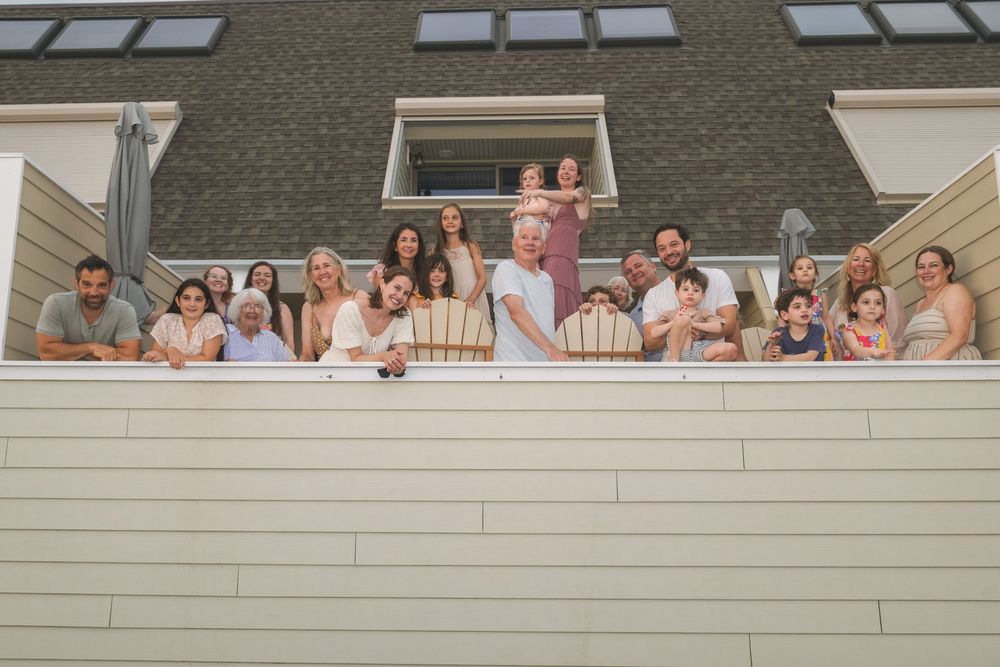 Groups of people smile and pose together on multiple connected balconies of a white building structure.
