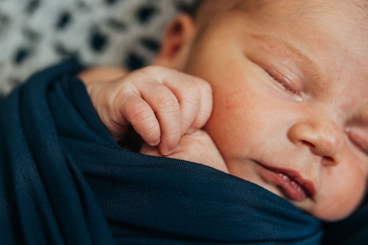 Tender moment between parent and sleeping infant in intimate indoor portrait.