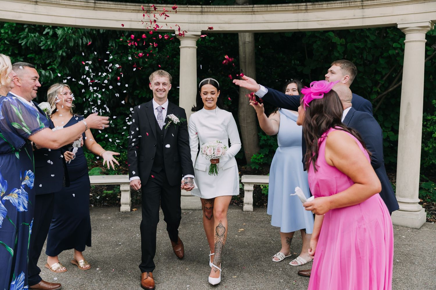 Wedding party celebrates under an outdoor colonnade with pink flower petals scattered on the ground.  Photographer. Hull. East Yorkshire.