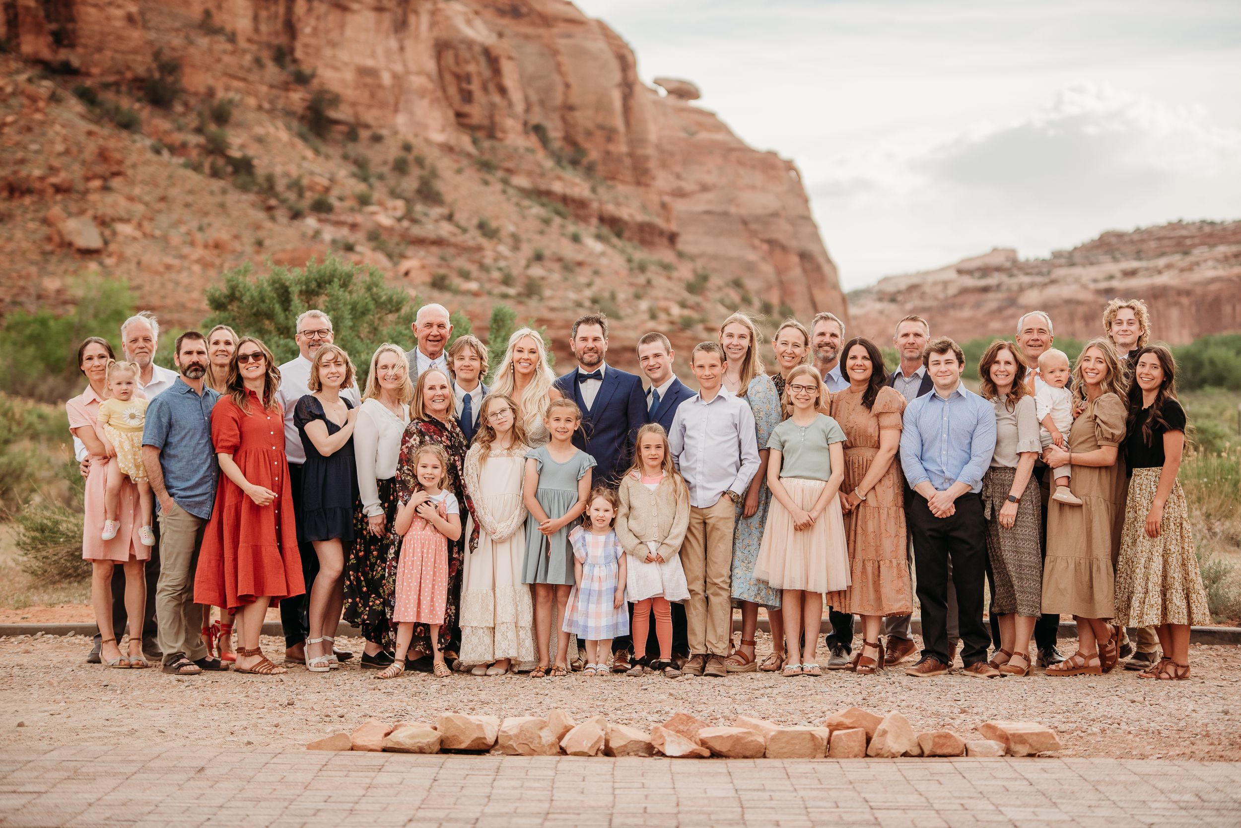 Large family group poses together for portrait in front of red rock formations in desert landscape.
