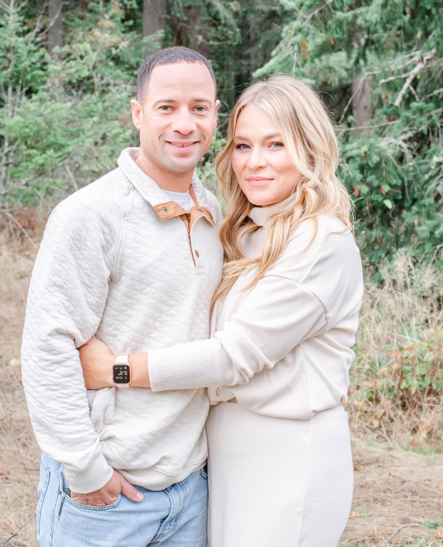 Couple in matching white sweaters embracing outdoors in natural setting.