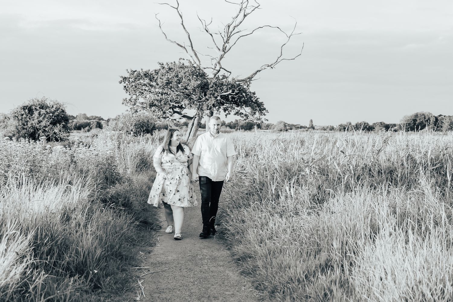 Couple walking along nature path through tall grass field.