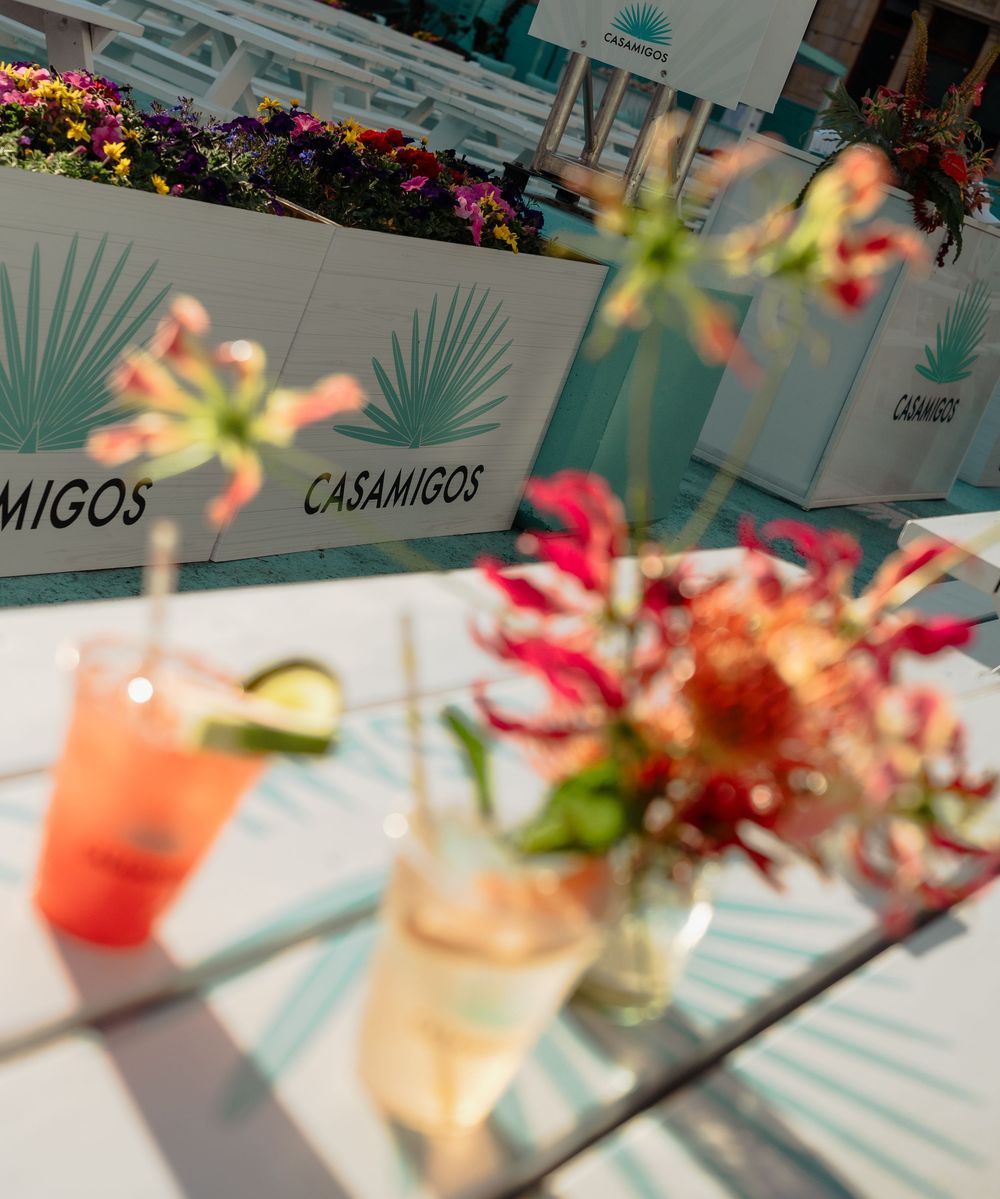 Casamigos tequila branded event with colorful cocktails and floral arrangements on a glass table outdoors.