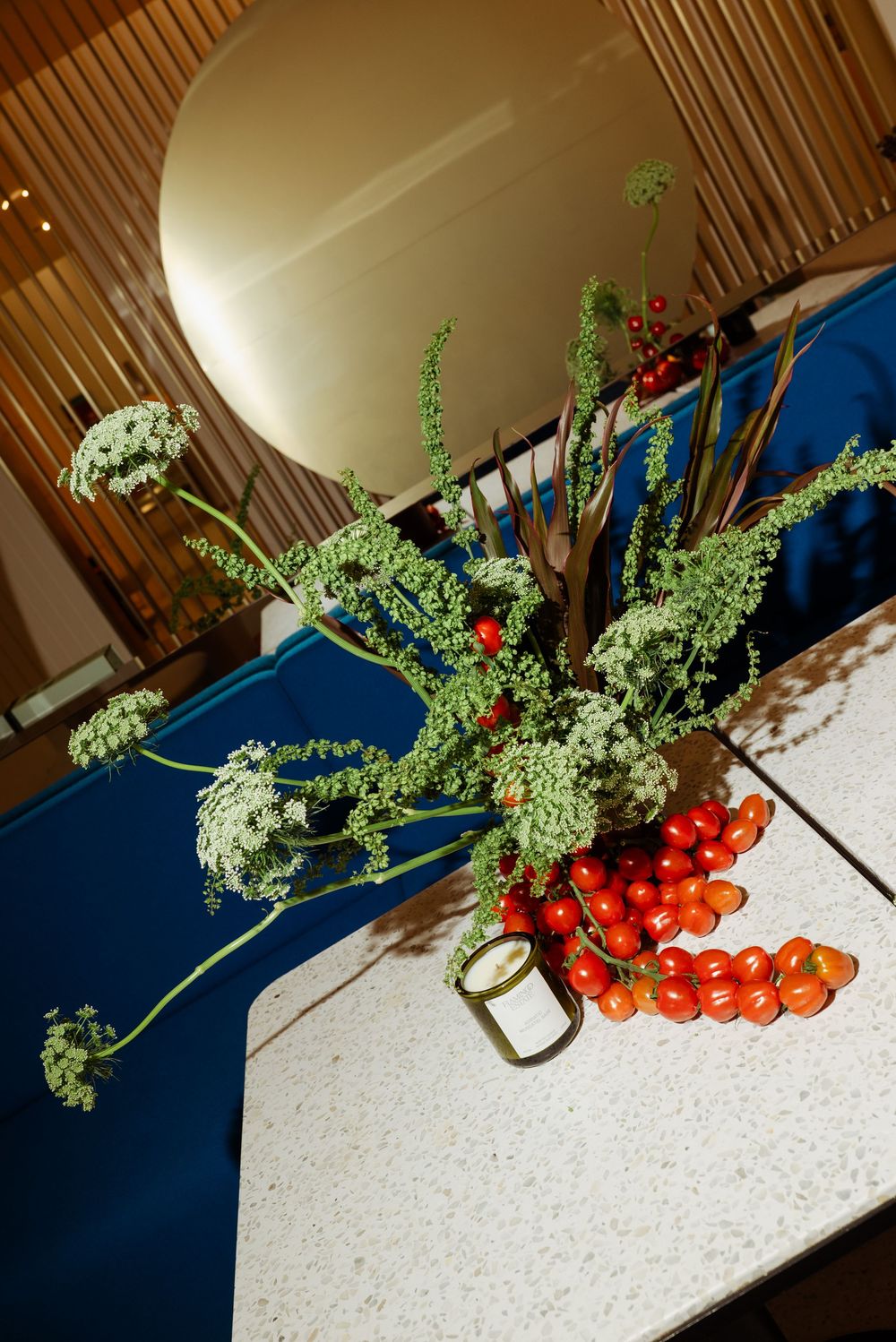 Floral arrangement with Queen Anne's lace, red berries, and cherry tomatoes on a white surface with blue table runner.