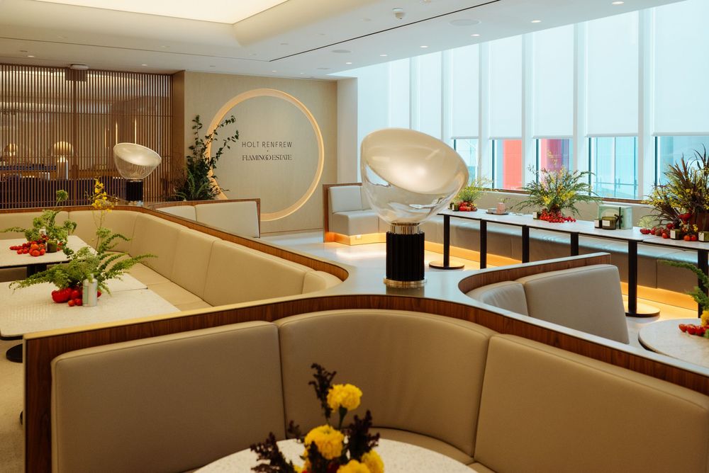 Modern airport lounge with curved cream booths, elegant lighting, fresh flowers, and panoramic windows offering city views.