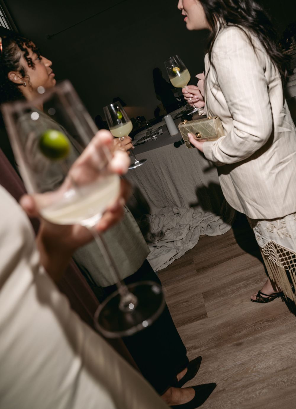 Guests mingling at an elegant party, holding wine glasses with white wine and lime garnish.