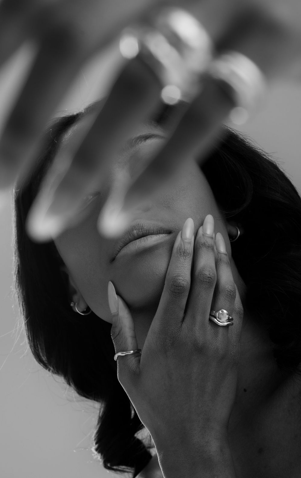Black and white close-up of hands with engagement ring covering face.