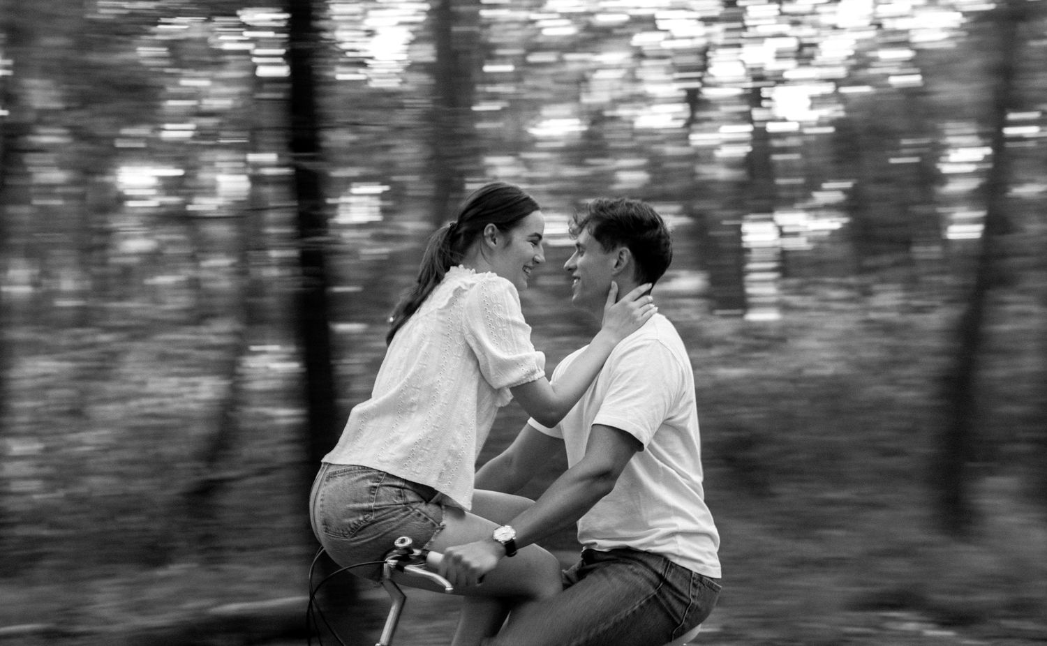 A romantic black and white photograph of a couple on a bicycle riding through a forest setting.