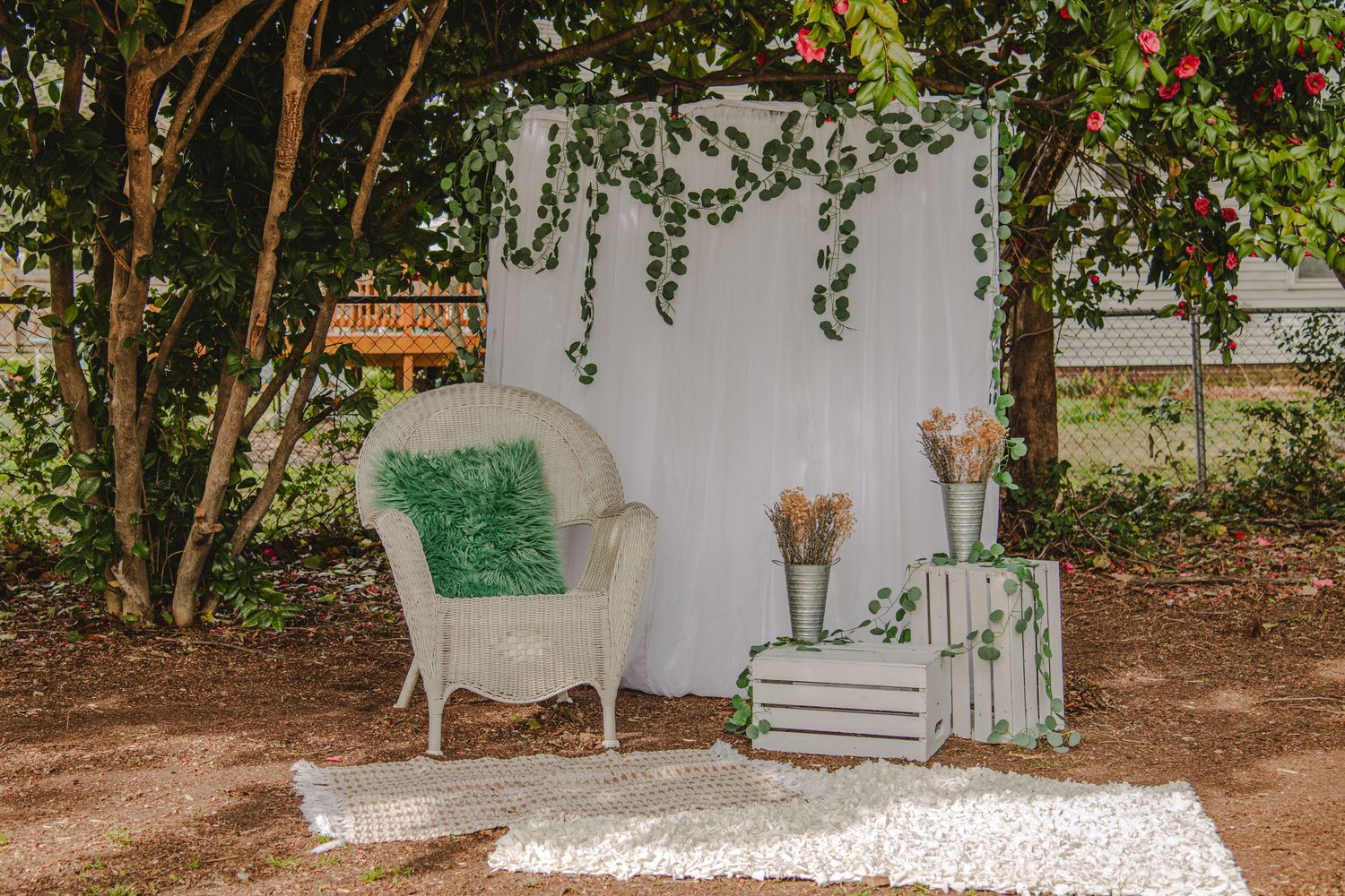 Romantic garden photo setup with white wicker loveseat, floral backdrop, and pink and mint green accents on grass.