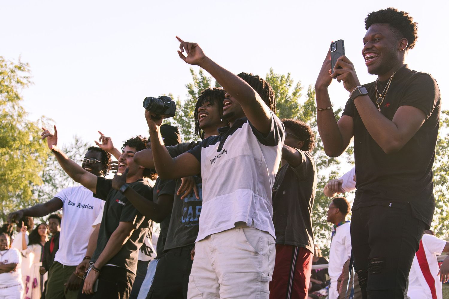 Crowd of young people celebrating outdoors at a street event, pointing and taking photos.