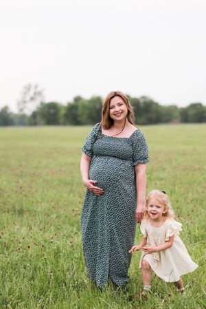 Mother and child playing together in a sunny meadow wearing floral and cream dresses.