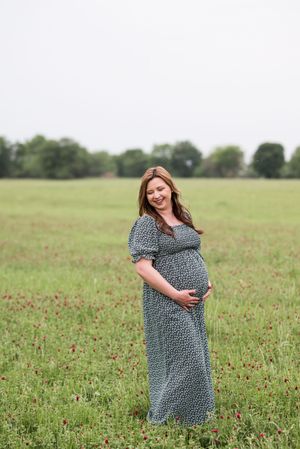 A pregnant woman in a patterned dress poses in a field of red wildflowers during a maternity photoshoot.