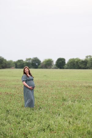 Person in a floral dress walking through a vast green field on a sunny day.