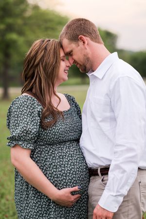 A couple shares intimate moments in a grassy field, with the woman wearing a floral print dress and man in white shirt.