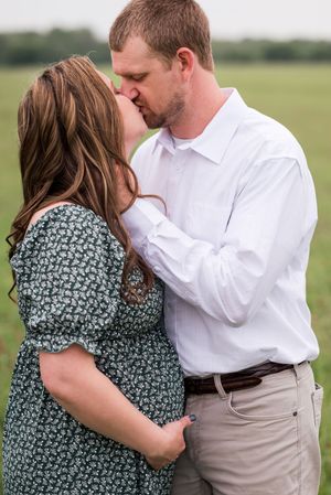Romantic couple embraces in a grassy field wearing coordinated white and floral outfits during an outdoor photoshoot.