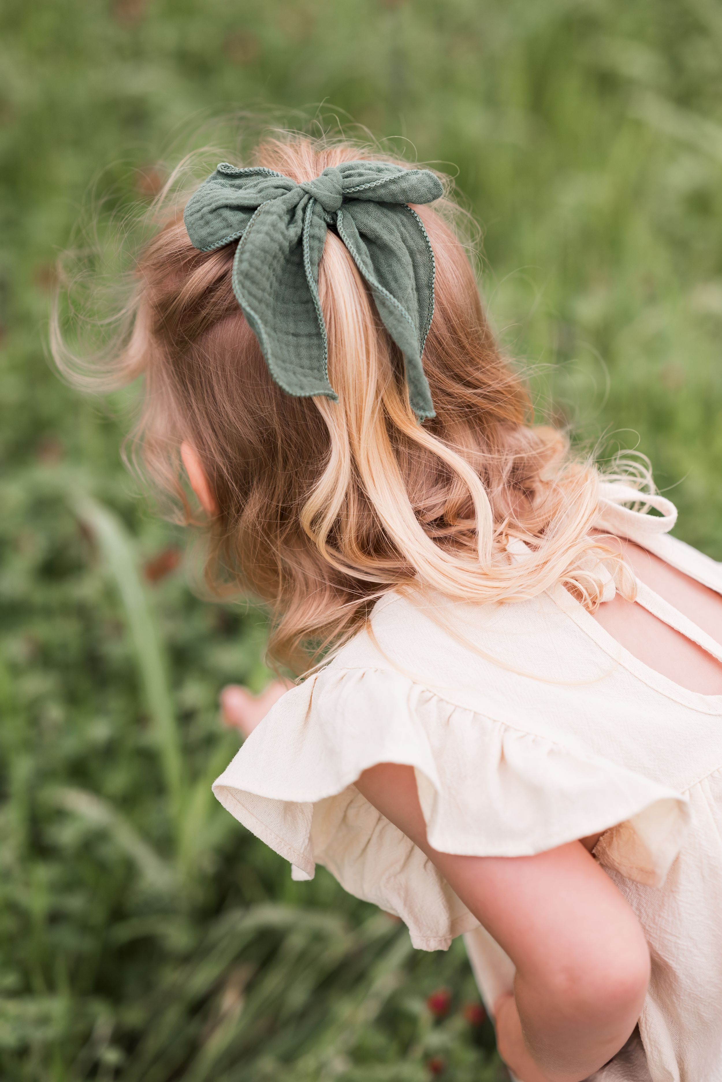 A series of playful hair flips showing a cream colored dress and green bow against a natural outdoor background.