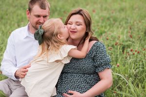 Family sitting together in a grassy field wearing casual summer clothing.