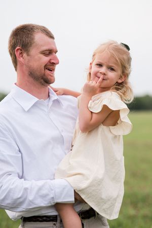 A playful moment captured in a grassy field with a white shirt and cream dress.