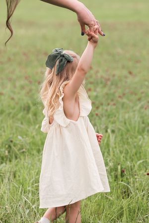 Young child in white dress twirling and playing joyfully in a sunlit grassy field.