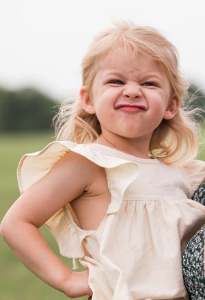 Candid expressions of a young child wearing a cream colored dress outdoors.