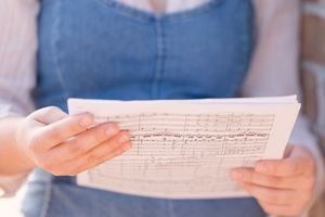Hands holding and examining a piece of handwritten sheet music against a blurred background.