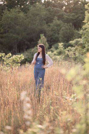 A dreamy outdoor photoshoot in a golden field with tall grass and soft sunlight filtering through the trees.
