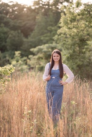 Ethereal portrait session in a rustic field with denim overalls and flowing sleeves against a natural backdrop.
