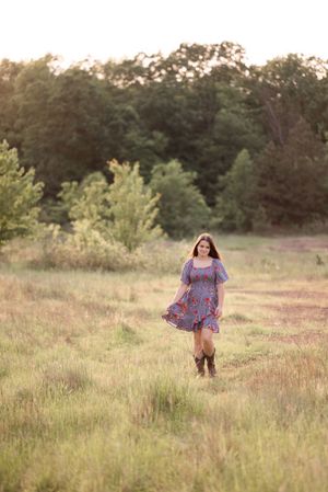 Whimsical outdoor photography in a summer meadow with flowing floral dress and warm evening light.
