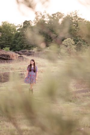 Artistic portrait through blurred foreground elements in a sun-drenched field during golden hour.