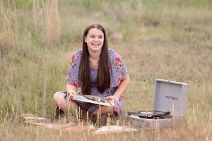 Someone wearing a floral dress sits in a grassy field while looking through a collection of photographs.