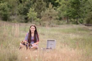 A person sits cross-legged in a grassy field with a record player and vintage vinyl records.