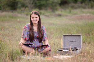 A person in a floral dress sits outdoors with a vintage record player and vinyl collection.