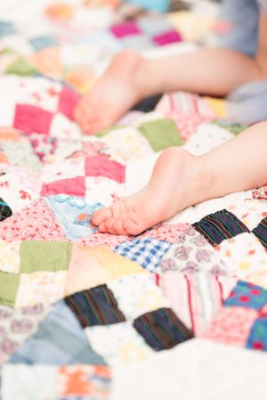 Close-up view of tiny feet resting on a colorful patchwork quilt.