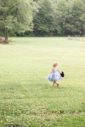 A child in a blue dress runs across a green field on a sunny day.