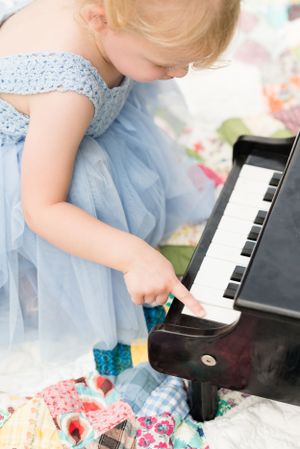 Small hands playing a toy piano while sitting on a colorful patchwork quilt.