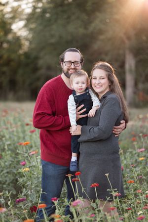 A couple embraces in a field of red wildflowers during sunset while wearing red and gray sweaters.
