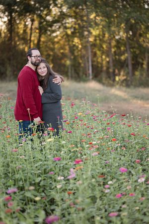 A couple embraces in a field of vibrant pink wildflowers during golden hour with trees in the background.