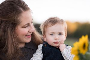 A parent and young child share a tender outdoor moment together near bright yellow sunflowers at sunset.