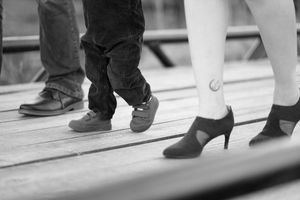 A black and white close-up photograph showing a row of people's feet and shoes walking on stairs.