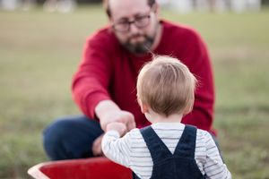 A person in a red sweater holds and plays with a small child on a grassy field.