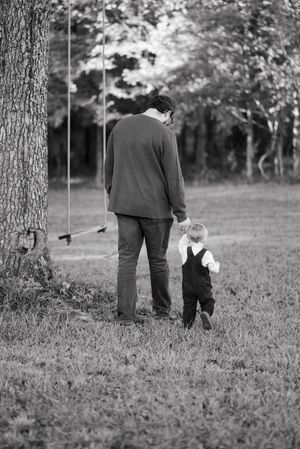A black and white photo of an adult and small child standing together near a tree in a grassy field.