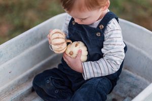 A small child in a navy vest plays while sitting in a vintage galvanized metal tub outdoors.