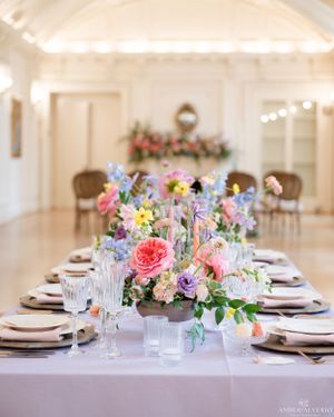 Elegant wedding reception table with pink and purple floral centerpiece and place settings.