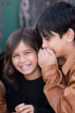 Two siblings share a playful moment together as one whispers and the other laughs joyfully.