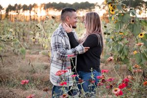 Romantic couple embracing in a flower field at sunset with red blooms surrounding them.