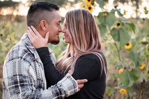 A couple embraces in a romantic outdoor photoshoot with sunflowers and natural lighting in the background.