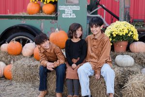 A seasonal fall photoshoot with pumpkins, hay bales, and yellow mums creating a festive autumn backdrop.