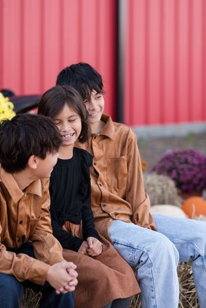 A group sits together on a wooden bench in front of a red barn wall during autumn.