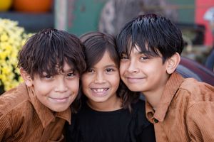 Three smiling children pose together in a close-up outdoor portrait.