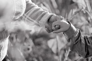 Black and white close-up of a small hand gently touching a flower in a garden setting.
